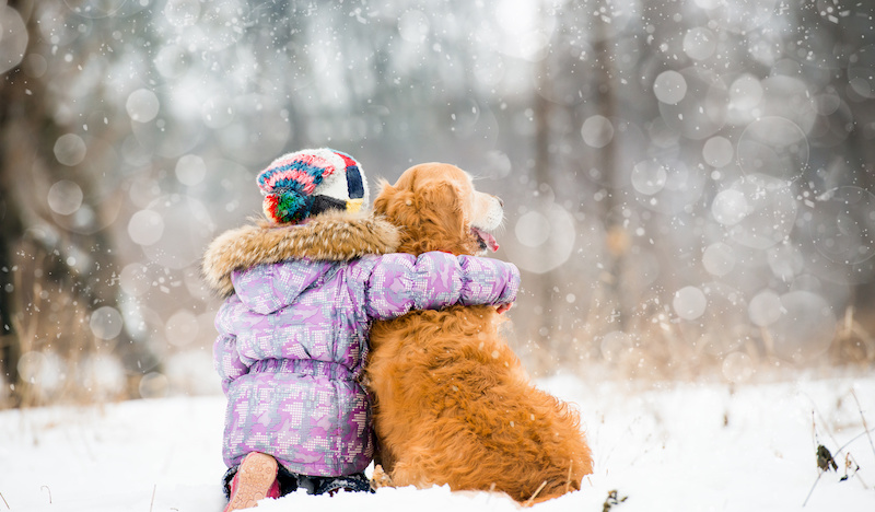 girl hugs dog in falling snow