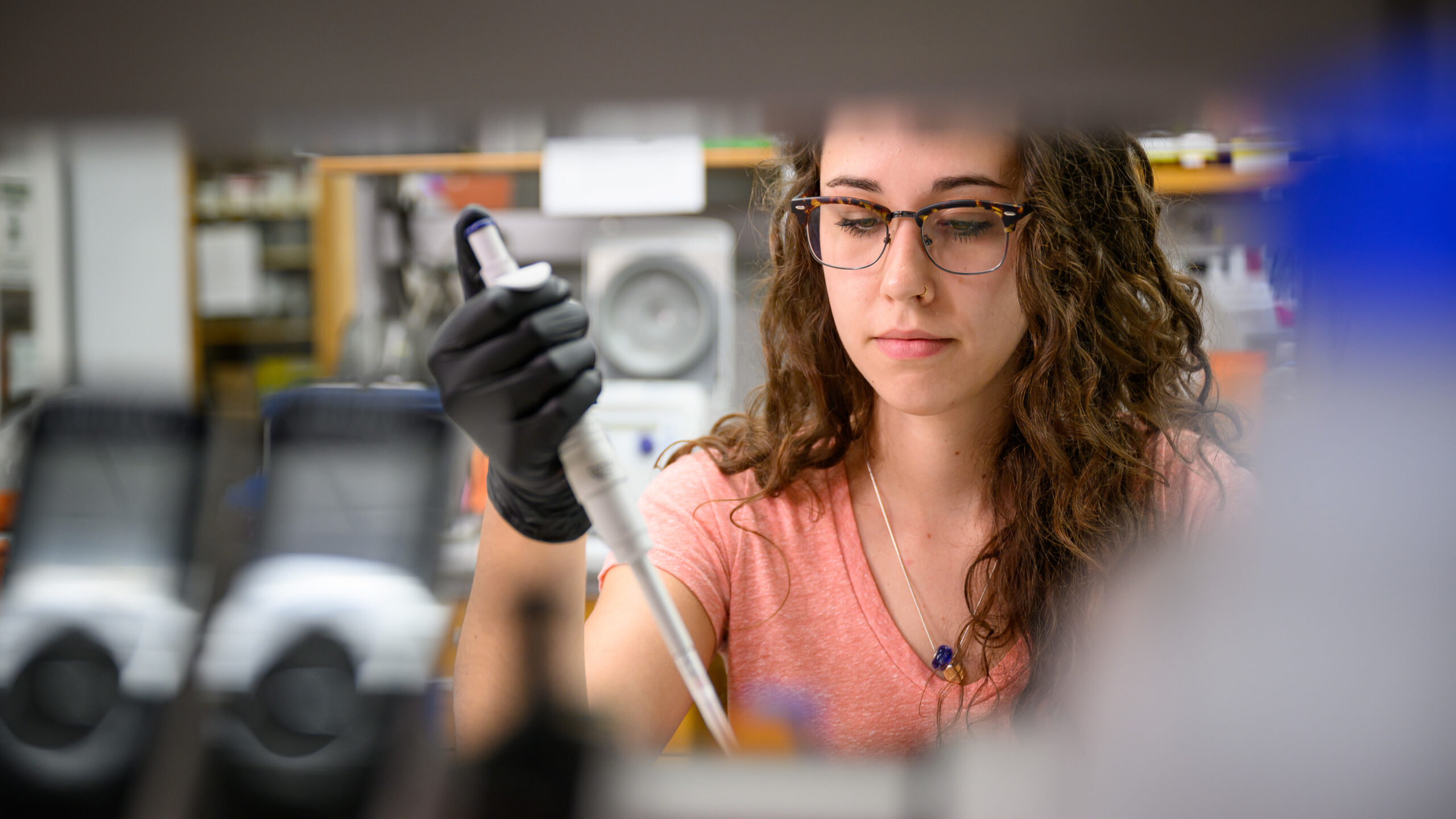 NC State College of Veterinary Medicine student Meg Mulder, wearing glasses, a pink shirt and black gloves, uses a dropper in the lab.