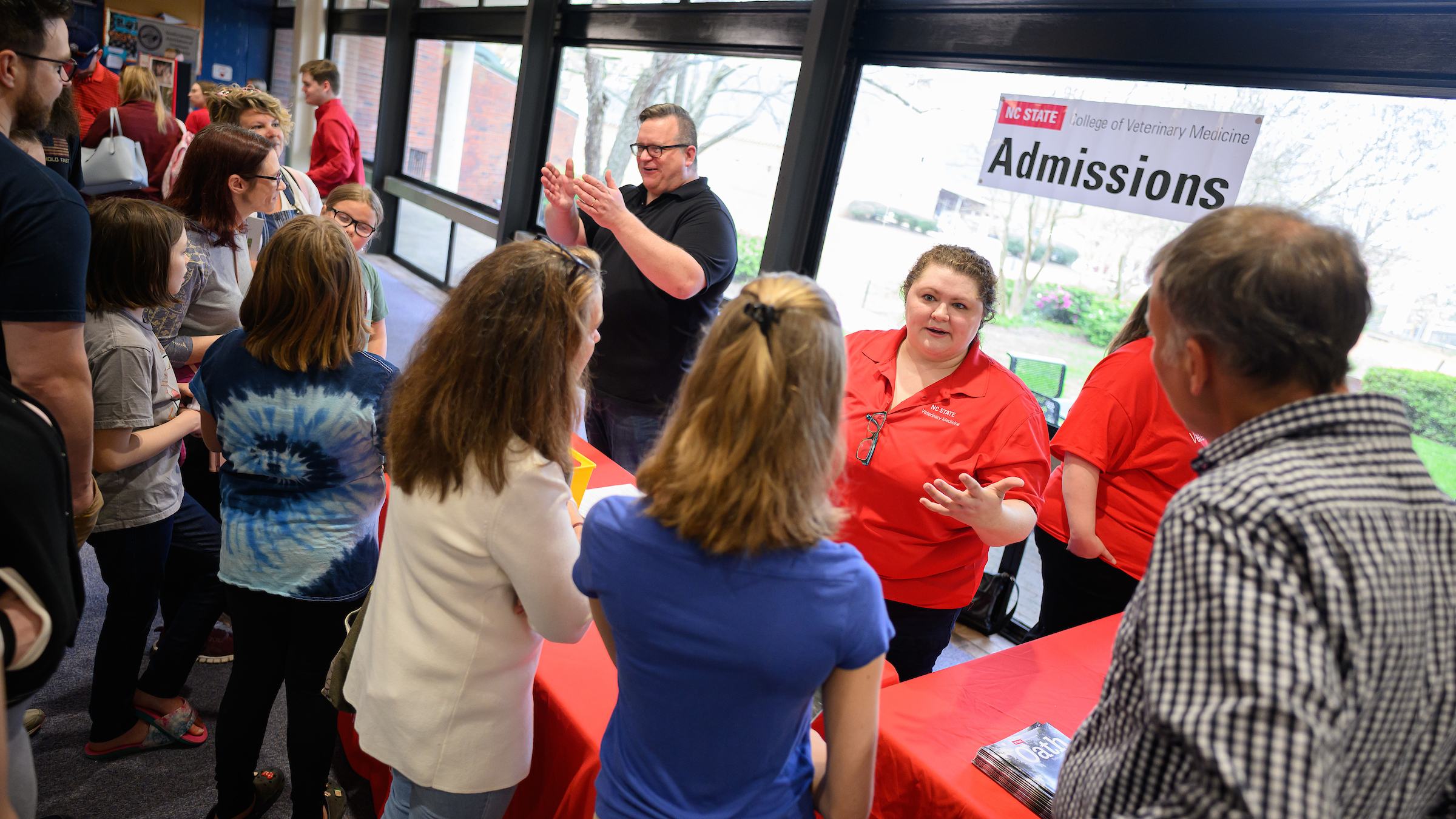 College admissions staff standing behind a table talk to families standing at an open house event.