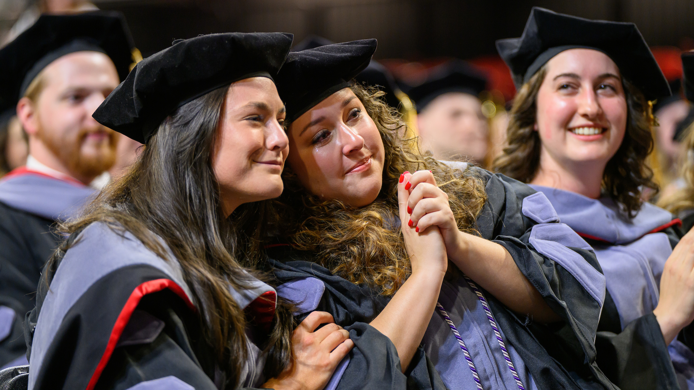 Two graduates lean into each other, hands clasped, at the NC State College of Veterinary Medicine's 2024 graduation.