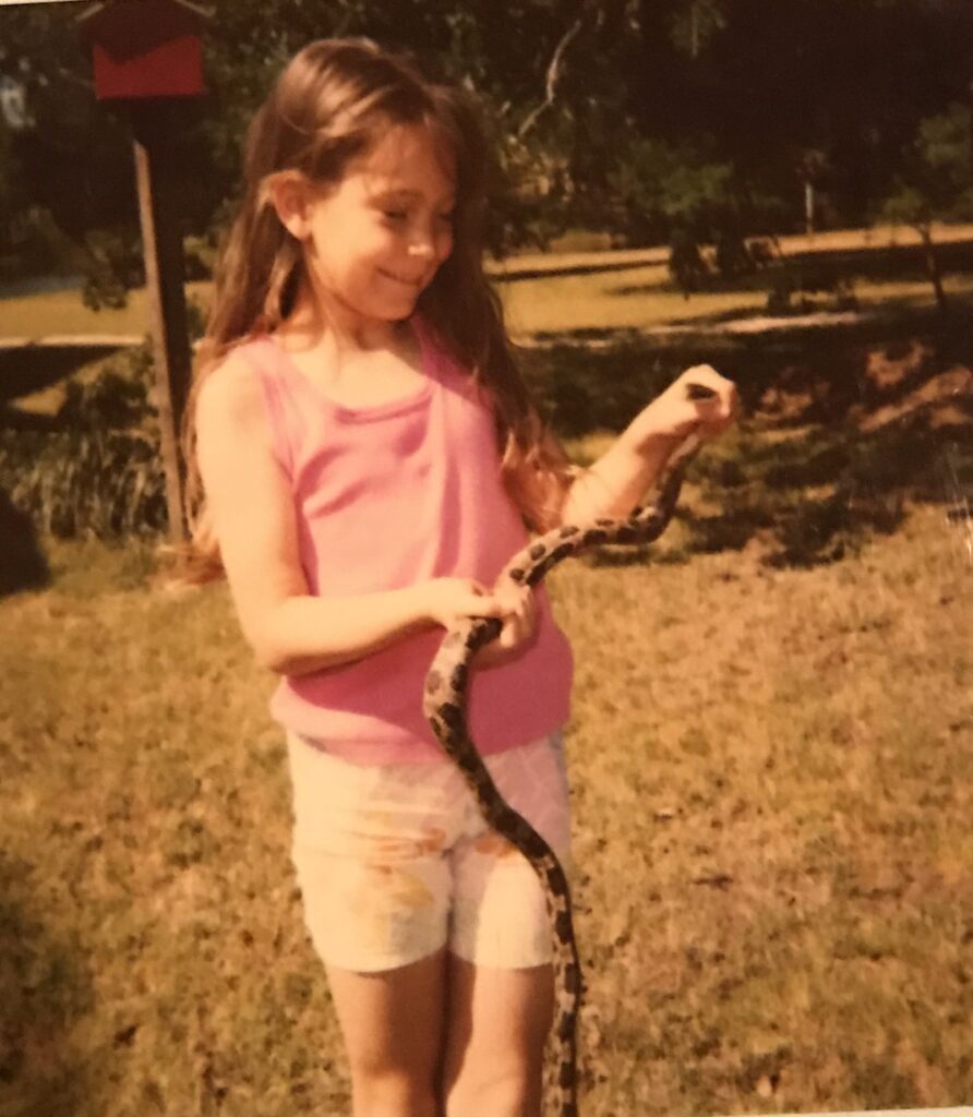 In an archive photo, a young Dr. Candace Wimbish, at around 6 years old, holds a spotted snake while outside in Texas.