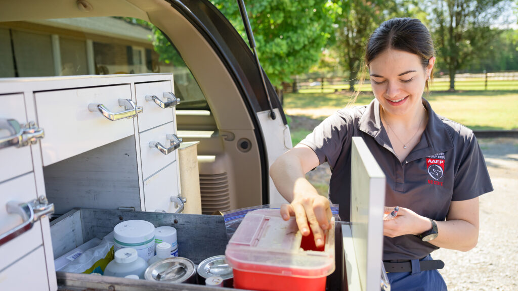 A veterinary student smiles as she packs vaccine syringes into an organizer in the back of a work truck.