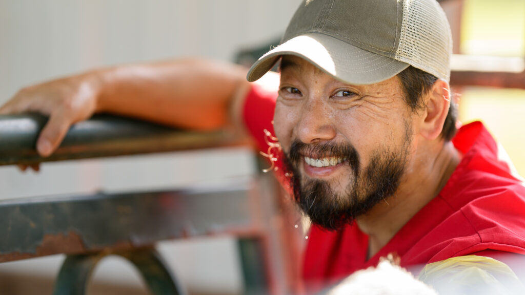 A male veterinary student smiles while performing a pregnancy check on a cow, not visible.