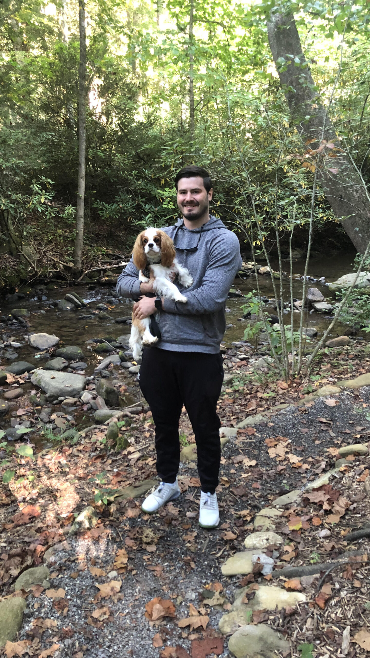 Seth Bowden, a male veterinary resident, holds a Cavalier King Charles spaniel dog while on a hike.