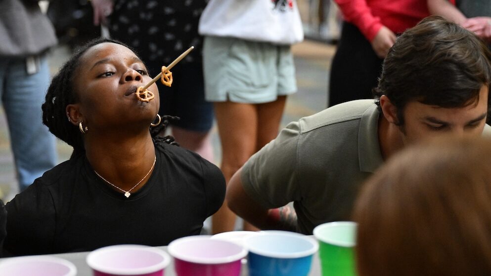 A student tries to put pretzels on a chopstick in her mouth.