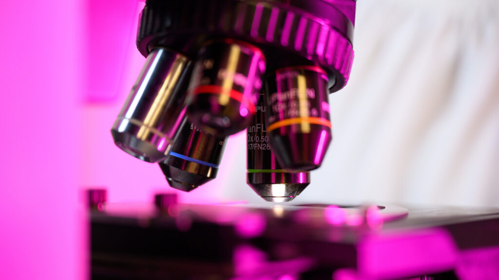 A close-up of a microscope lit with purple lighting.