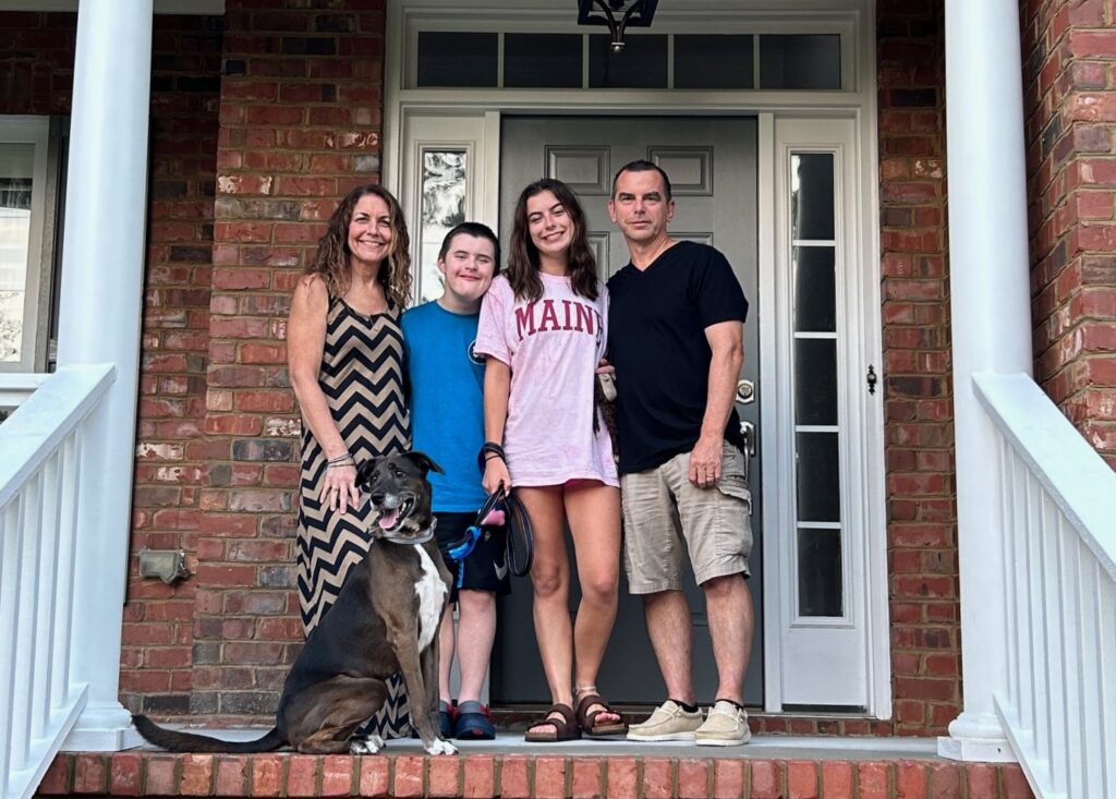 Members of the Krebs family stand on their porch, smiling at the camera with Zuzu.