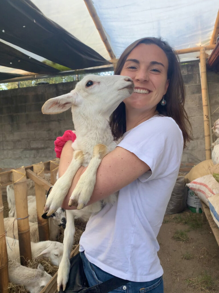 Siena Mitman smiles at the camera while holding a white lamb.