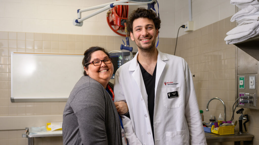 Veterinary technician Tammy Buck poses with Pinto, holding onto his arm and grinning, during a day in the clinic. 