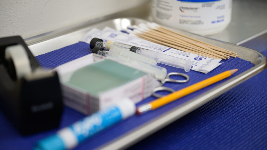 A collection of medical equipment, including vials and microscope slides, sits on a table in the dermatology clinic where Pinto works.