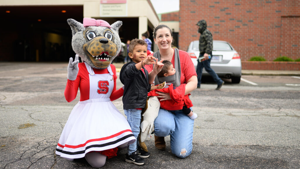 A mother poses with her two young children next to NC State mascot Ms. Wuf.