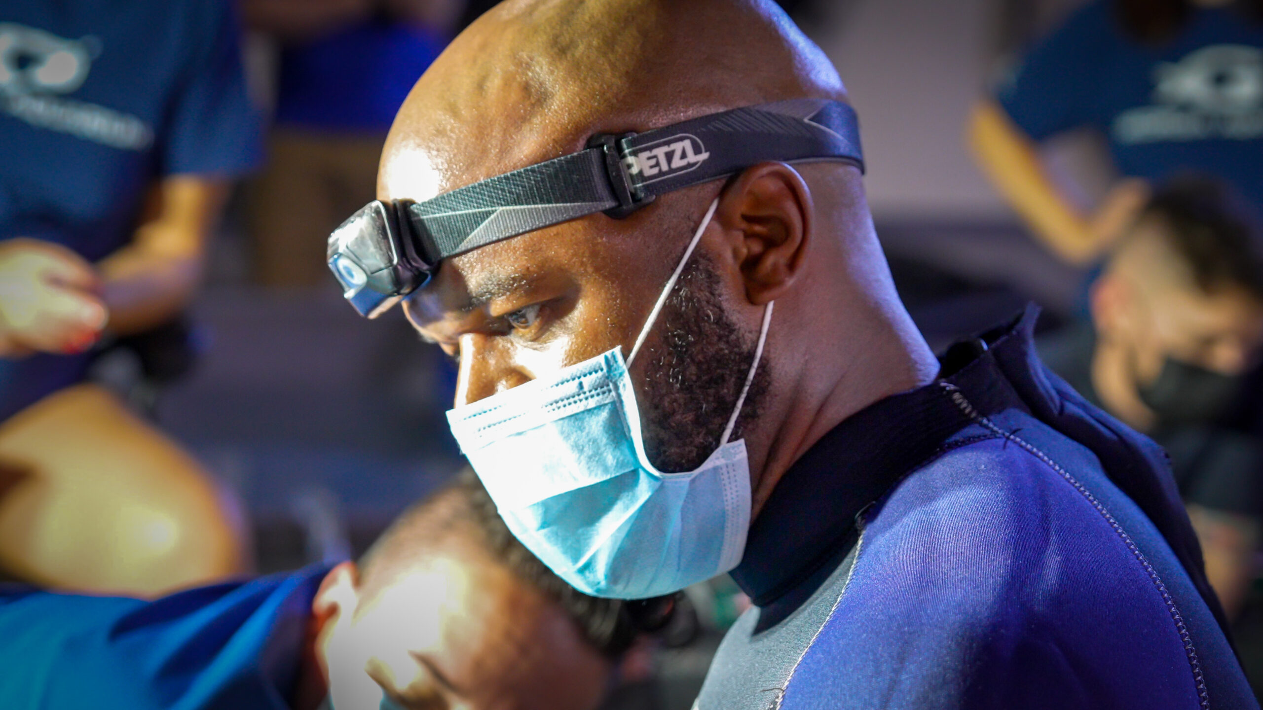 A side profile photo of Dr. Greg Scott. He is wearing surgical garb, including a face mask and a headlamp.