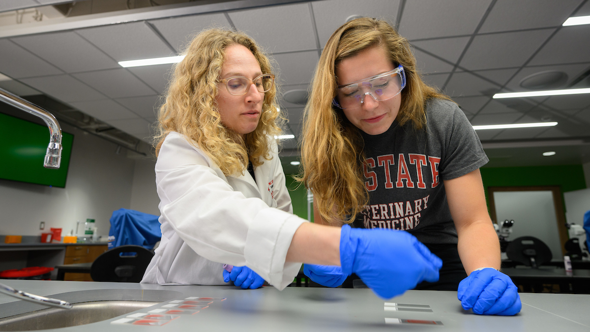 Dr. Devorah Stowe in a white lab coat works with a student in a lab