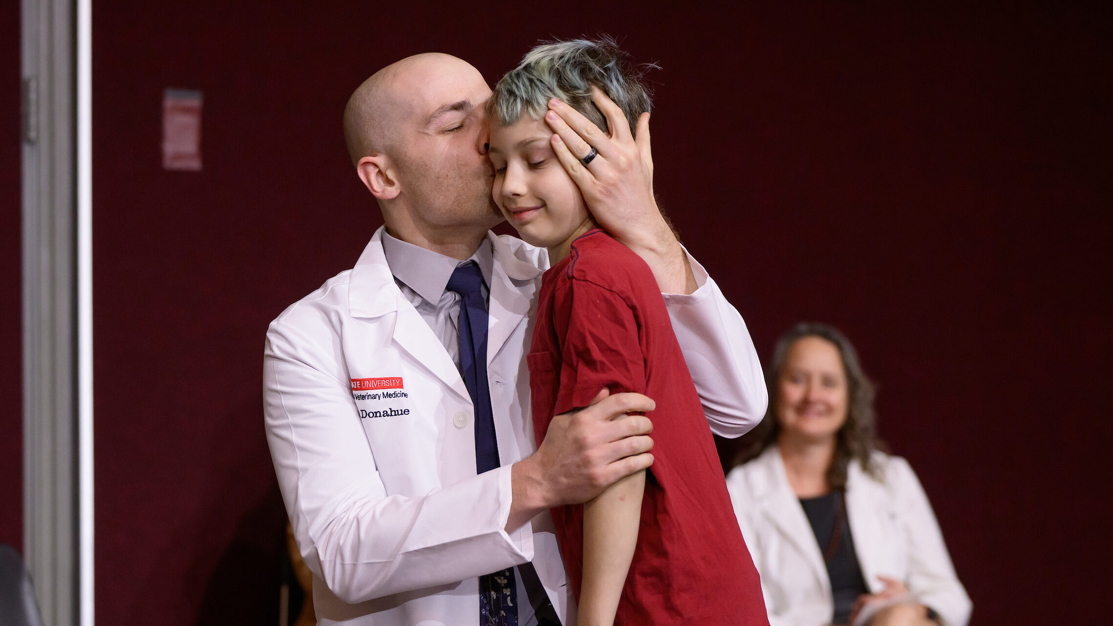 Third-year student, Blake Donahue kisses his son's forehead after he bestows his father's white coat