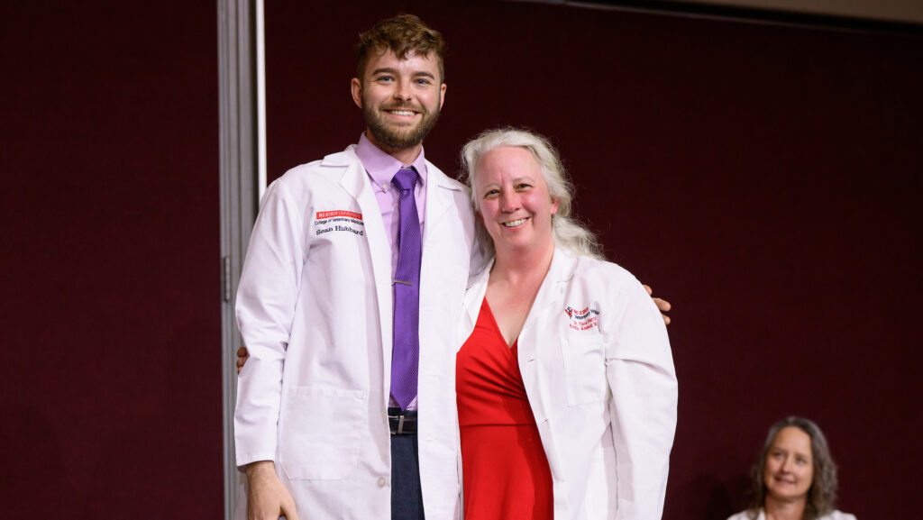 Third-year student, Sean Hubbard and Dr. Tara Harrison pose for a photo after Dr. Harrison puts on Sean's white coat.