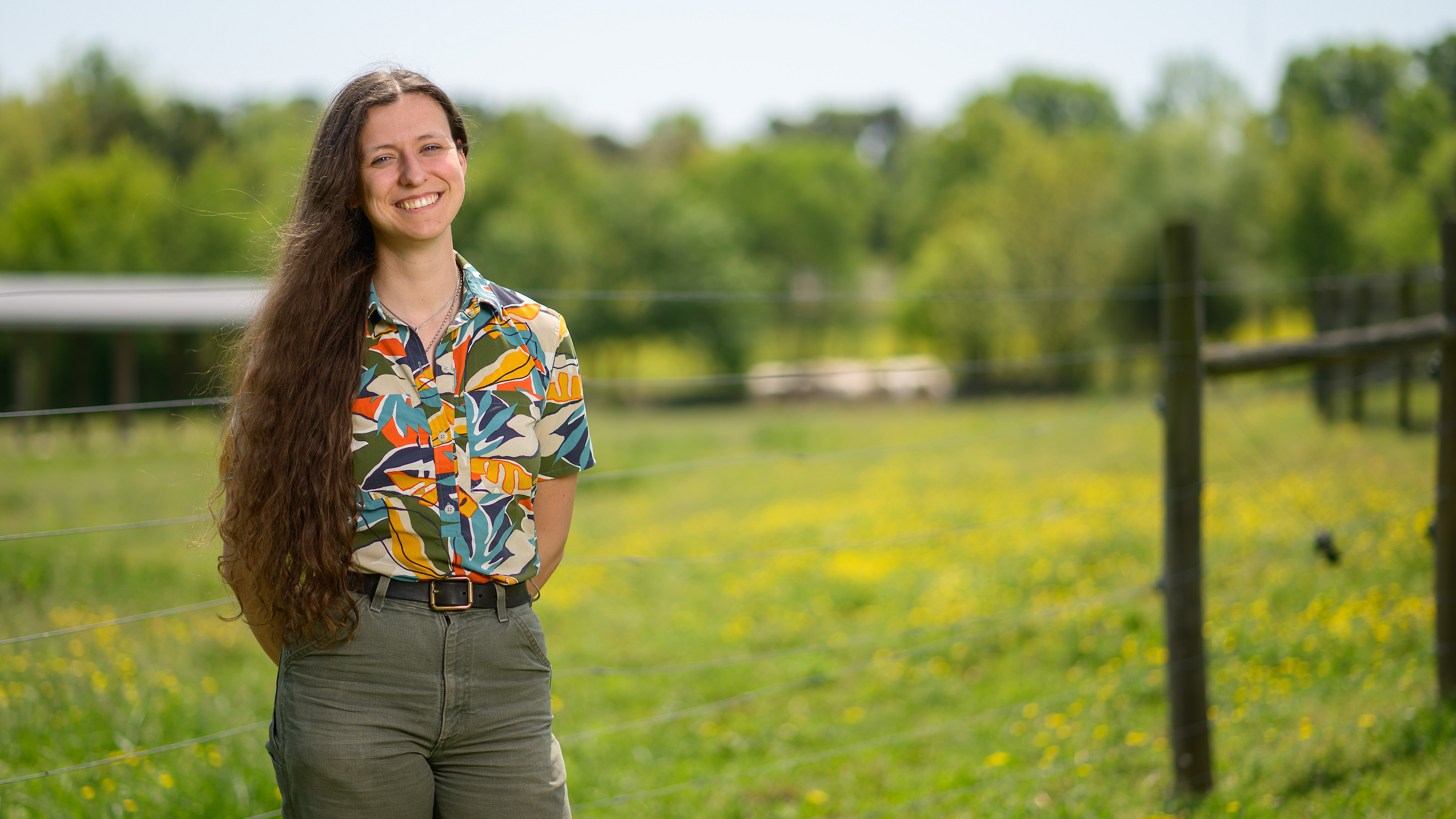 Class of 2025 grad Maya Keefer stands in front of a field at the NC State College of Veterinary Medicine.