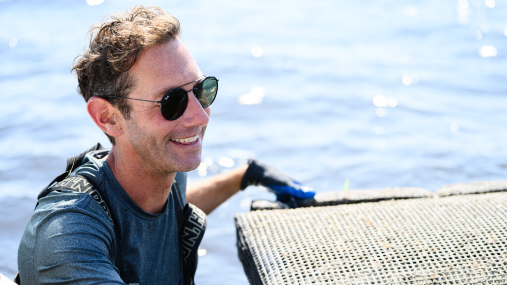 Dr. Tal Ben-Horin, in blue shirt and sunglasses, relocates a set of oyster bags from CMAST to Core Sound as part of a study into the disease resistance of different genetic lines of oyster.