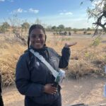 aniya smiles and holds her hand up towards a group of elephants off in the distance