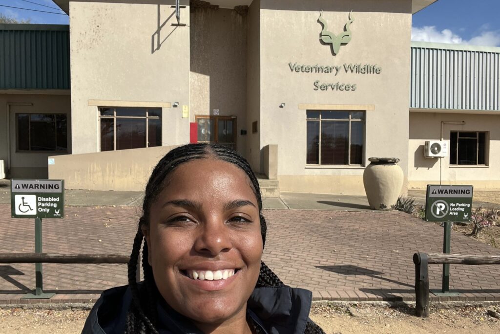Aniya takes a smiling selfie with a building that reads "Veterinary Wildlife Services"