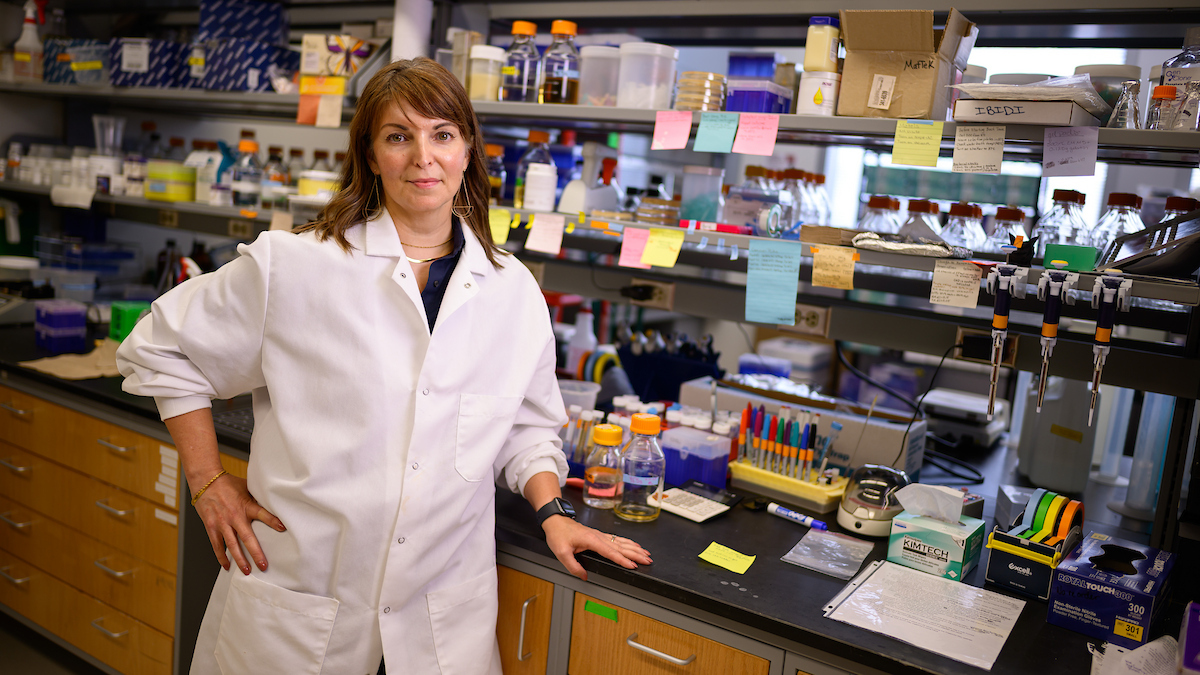 Dr. Caroline Laplante in white lab coat stands with her hand on hip in her lab