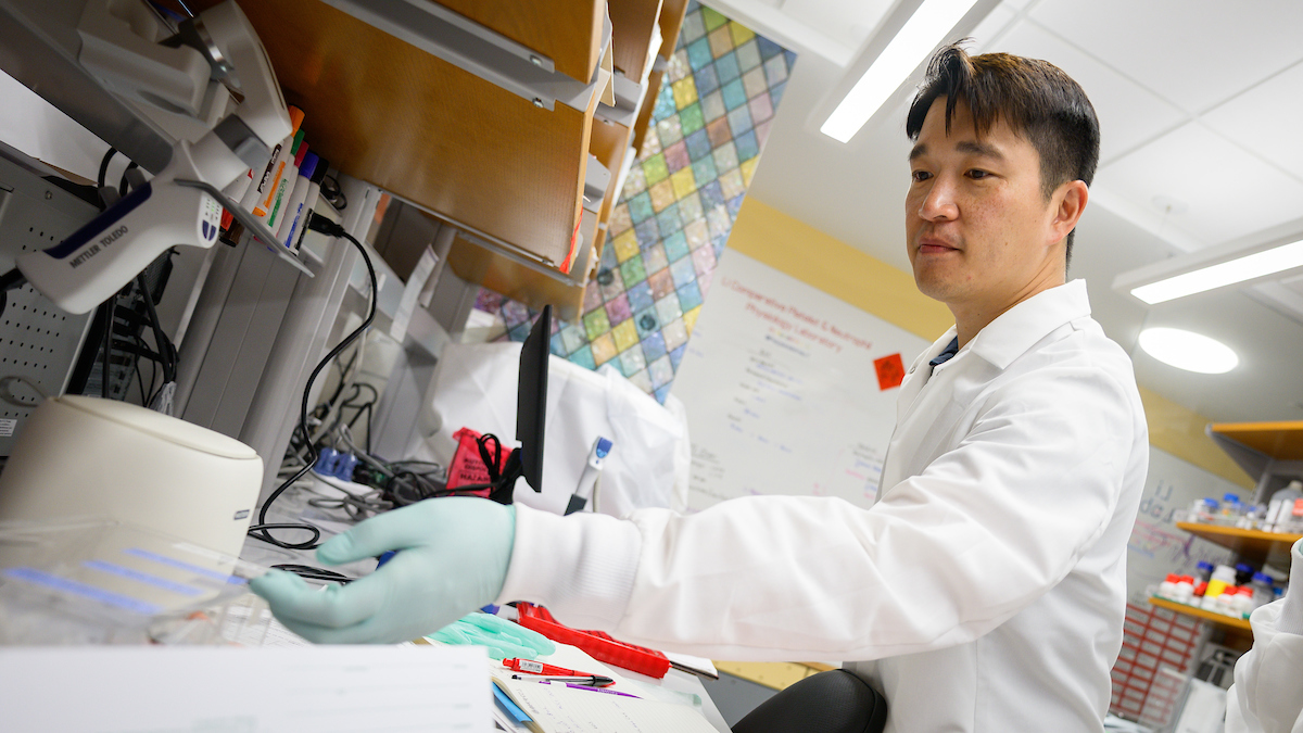 Dr. Ron Li wearing a white lab coat with blue gloves in a lab